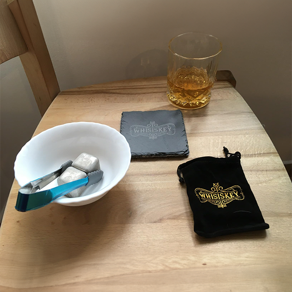 single_whiskey_tumbler_with_whiskey_cooling_stones_and_slate_coaster_on_table